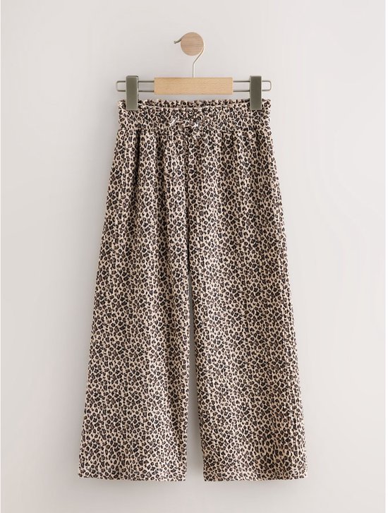 Beige wijde broek met panterprint en strikdetail aan de voorkant, hangend aan een kledinghanger.
