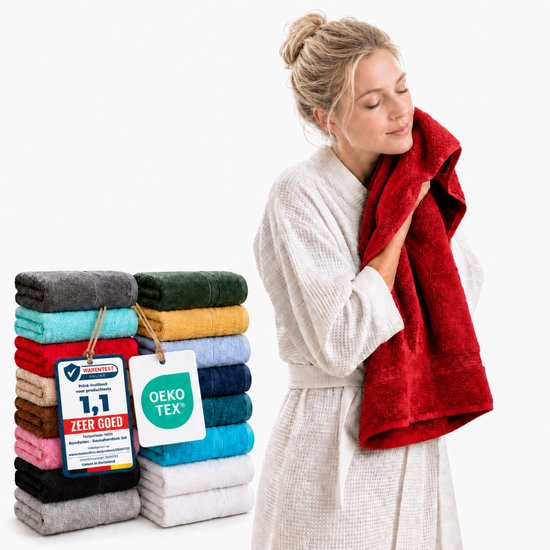 Femme blonde en robe de chambre se sèche le visage avec une serviette rouge, à côté d'une pile de serviettes colorées avec le label Öko-Tex.