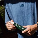 Blauwe longsleeve met klein blauw logo op de borst. Een persoon houdt een groene zonnebrandcrème fles vast.