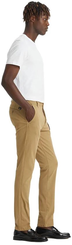Man in een beige chino broek, staand met de hand in de zak.