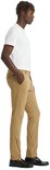 Man in een beige chino broek, staand met de hand in de zak.