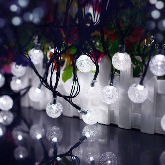 Een lichtsnoer met veel transparante lichtballetjes in koude witte tinten, met reflecties op een donkere ondergrond.