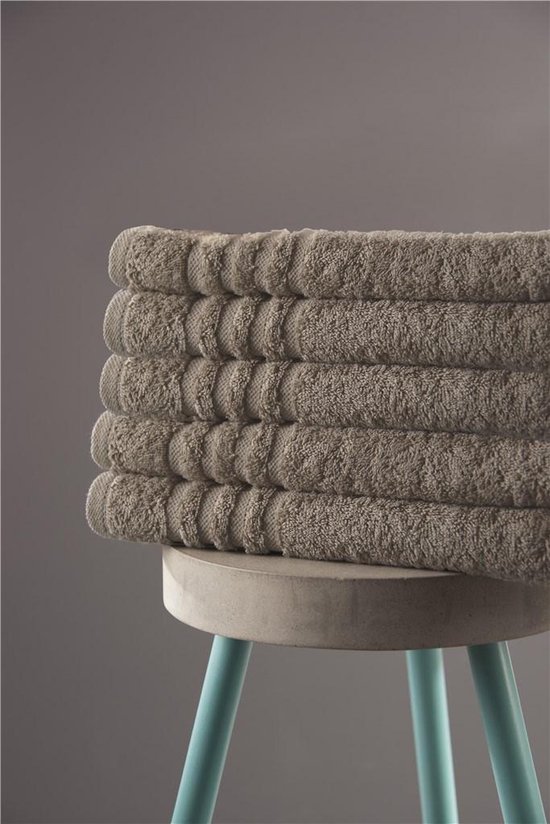 Pile de serviettes taupe avec détail côtelé sur un tabouret en béton.