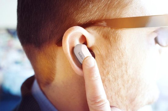 Close-up van een oor met een lichtgrijs Belkin oordopje, aangeraakt door een vinger.