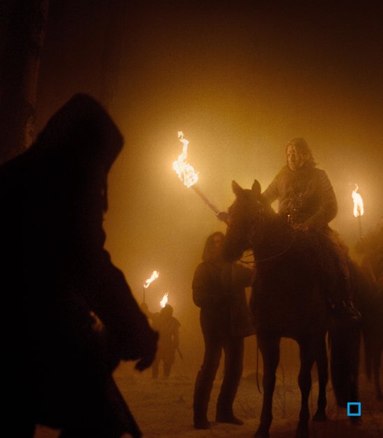 Een groep mensen met fakkels in het donker, een persoon te paard, in een mistige, besneeuwde omgeving.