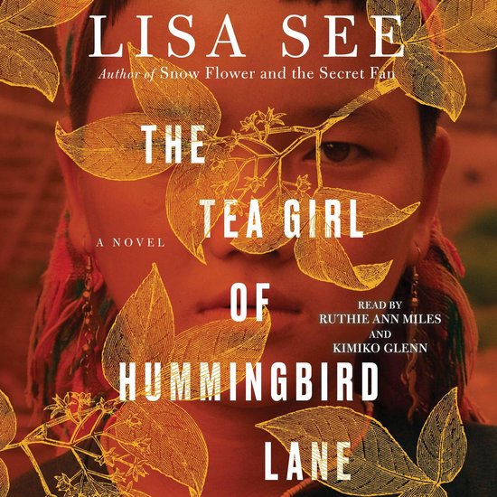 Boekcover van "The Tea Girl of Hummingbird Lane" door Lisa See. Een vrouw kijkt naar de camera, met oranje bladeren en takken eroverheen.