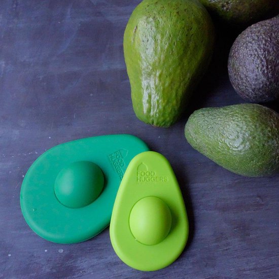 Twee groene avocado-vormige bewaardozen, met meerdere hele avocado's op de achtergrond.