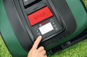Hand die de robotmaaier bedient via het bedieningspaneel met rood stop-bord.