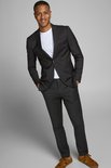 Jonge man met donkere huid draagt een zwarte Jack & Jones blazer met een wit T-shirt en zwarte broek, handen in de zakken.