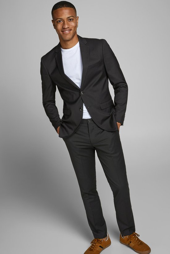 Jonge man met donkere huid draagt een zwarte Jack & Jones blazer met een wit T-shirt en zwarte broek, handen in de zakken.