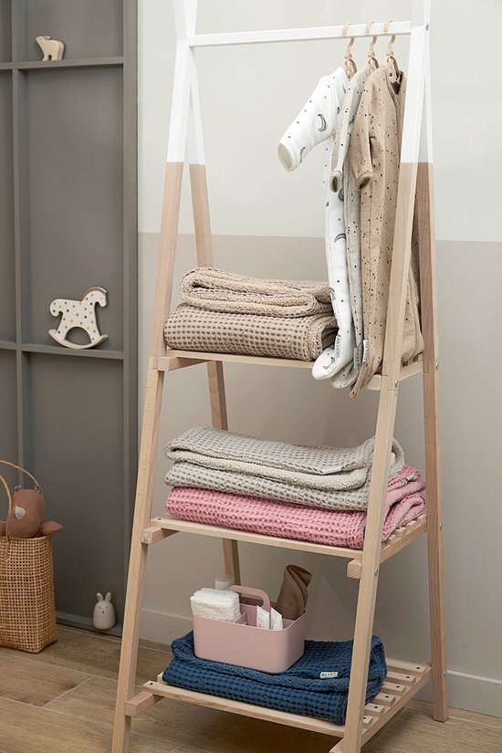 Houten kledingrek met hangende beige babyslaapzakken en gestapelde dekens in beige, roze en blauw.