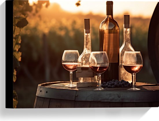Wijnglazen en flessen gevuld met rode wijn staan op een houten vat in een wijngaard bij zonsondergang.
