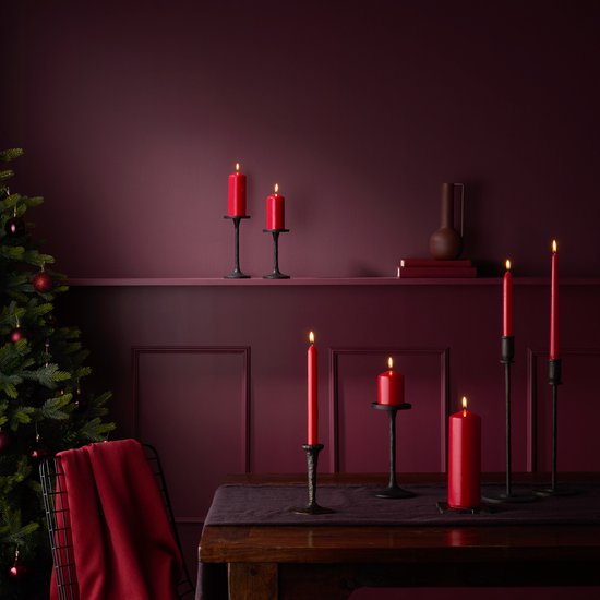 Rode kaarsen op donkere kandelaars naast een kerstboom en rode sprei.