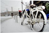 PVC Schuimplaat- Fiets Geparkeerd in Stad tijdens Sneeuwbui - 90x60 cm Foto op PVC Schuimplaat