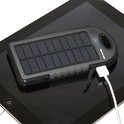 Zwarte zonnepaneel powerbank aangesloten op een tablet.