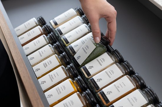 Hand pakt een kruidenpotje uit een lade met kruidenorganizer.