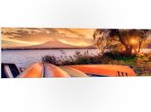 PVC Schuimplaat- Oranje Kano's op zijn Kop aan het Water tijdens Zonsondergang - 120x40 cm Foto op PVC Schuimplaat