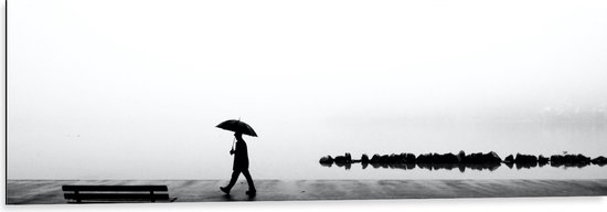 Dibond - Man met Paraplu Lopend langs Water op Mistige Dag (Zwart-wit) - 120x40 cm Foto op Aluminium (Wanddecoratie van metaal)