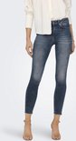 Model met blauwe skinny jeans met raw-edge enkelbroekspijpen en een lichte wassing.
