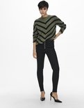 Model met olijfgroene trui met zwarte V-strepen en zwarte hoge broek.