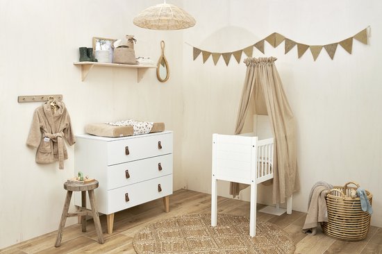 Kinderkamer met commode, luiertafel, wiegje met zandkleurige voile en kleding aan de muur.