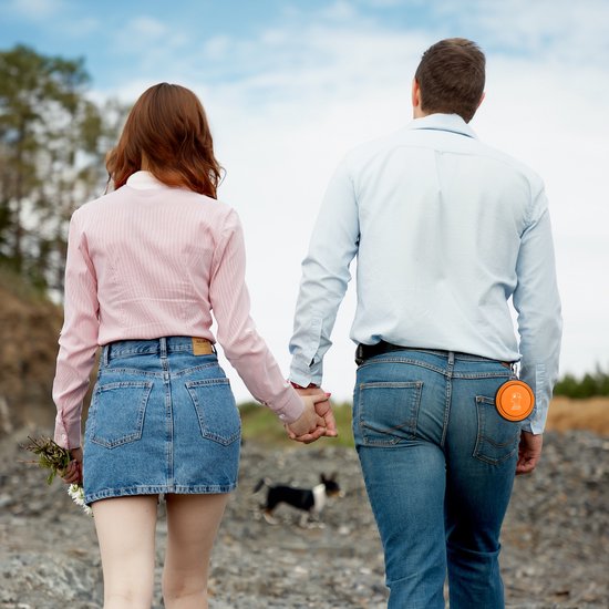 Een koppel dat hand in hand wandelt, met op de broek van de man een oranje opvouwbare voerbak.