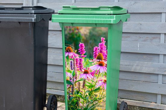 Groene afvalcontainer met sticker van roze echinacea en siergras, naast een grijze container.