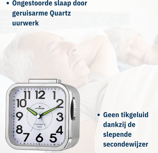Close-up van een zilverkleurige vierkante wekker met witte wijzerplaat, zwarte cijfers en groene wijzers. De tekst vermeldt "Geen tikgeluid" en "Geruisarme Quartz uurwerk".