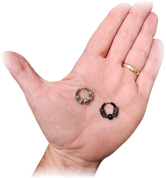 Deux boucles d'oreilles argentées et noires avec des détails de crânes sur une paume.