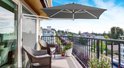 Donkergrijze rechthoekige muurparasol, geopend, boven een balkon met twee stoelen en uitzicht op huizen.