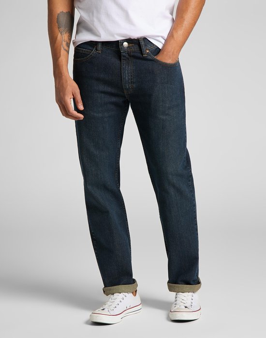Man in donkerblauwe Lee jeans met omgeslagen pijpen en witte sneakers, zak in de broek.