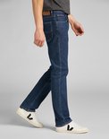 Man loopt in een rechte, donkerblauwe jeans met Lee-logo op de achterzak en leren patch.