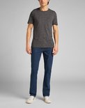 Man in een donkerblauwe jeans met rechte pijpen, met een grijs T-shirt met borstzakje.