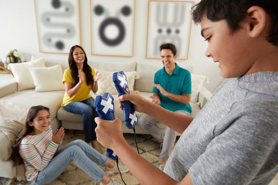 Un garçon tient des manettes de jeu bleues, une famille regarde dans le salon.