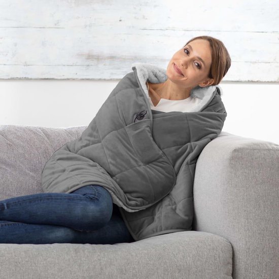 Vrouw glimlachend, gehuld in een grijze, zachte gewatteerde deken met teddy voering.