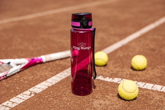 Transparante paarsrode drinkfles van 1 liter op een bruin tennisveld, met tennisracket en ballen.