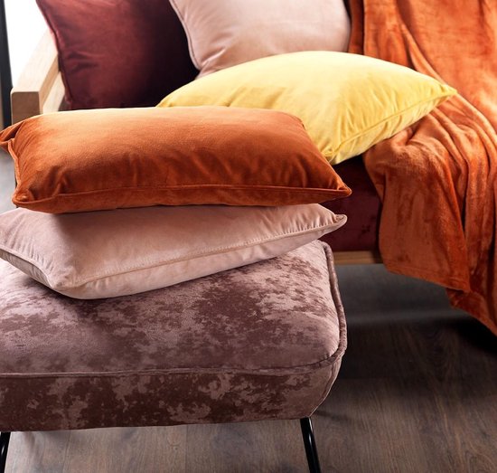 Pile de coussins en velours marron, rose, orange et jaune, sur un fauteuil et un pouf.
