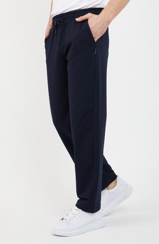 Man in donkerblauwe joggingbroek en witte sneakers, lichte buiging van het been.