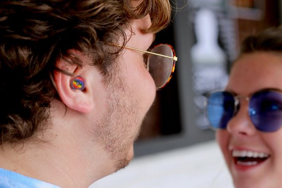 Man met zonnebril en een regenboog gekleurd oordopje in zijn oor, kijkend naar een vrouw.