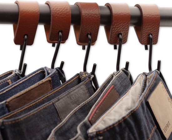 Bruine leren lussen met zwarte s-haken die jeans ophangen aan een zwarte staaf.