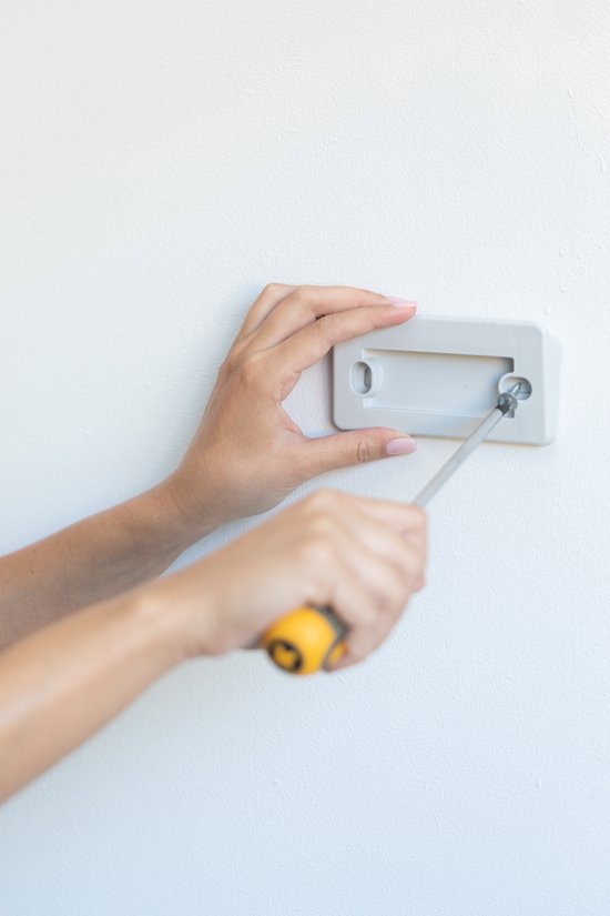 Mains grises avec vernis jaune vissant un support à un mur blanc.
