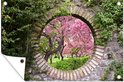 Une affiche de jardin avec un passage circulaire en pierre révélant des arbres roses en fleurs, montrant un coin retourné.