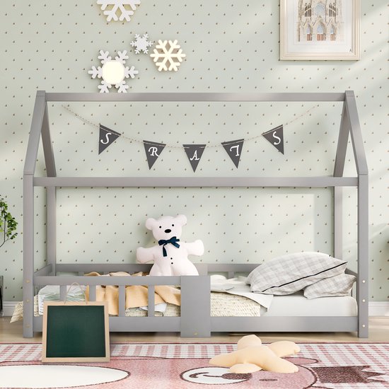 Grijs houten huisbedframe met hekjes, slingers, teddybeer, een matras en een kinderkamer vloerkleed.