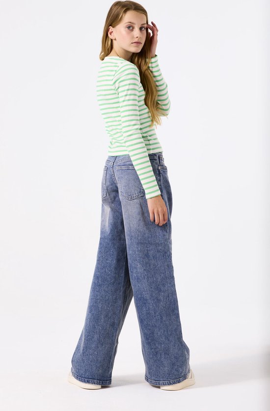 Meisje in groen gestreept shirt met lange mouwen en wijde jeans, gezien vanaf de zijkant.