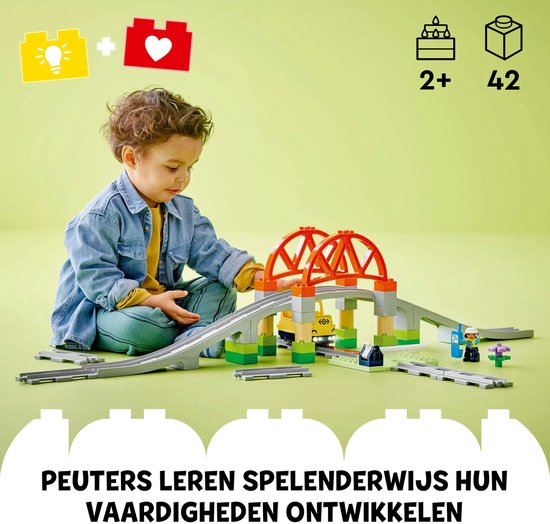 Kind bouwt met LEGO Duplo treinbrug en rails. Grijze spoorrails, oranje brug, overweg en figuren.