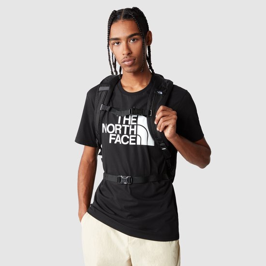 Man draagt zwarte The North Face rugzak over een zwart t-shirt met logo.