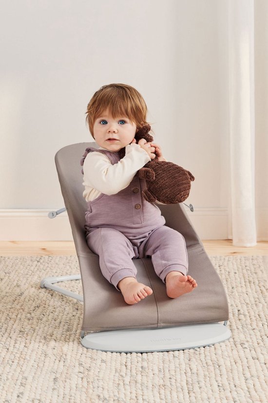 Baby in zandgrijs wipstoeltje met een bruine knuffel.