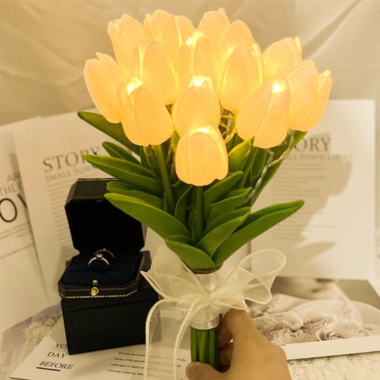 Boeket van 12 gloeiende gele tulpen met groene bladeren en witte strik. Een trouwring in een open zwarte doos staat ernaast.