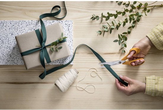 Handen knippen een groen lint met een Fiskars schaar met oranje handgrepen op een houten tafel.
