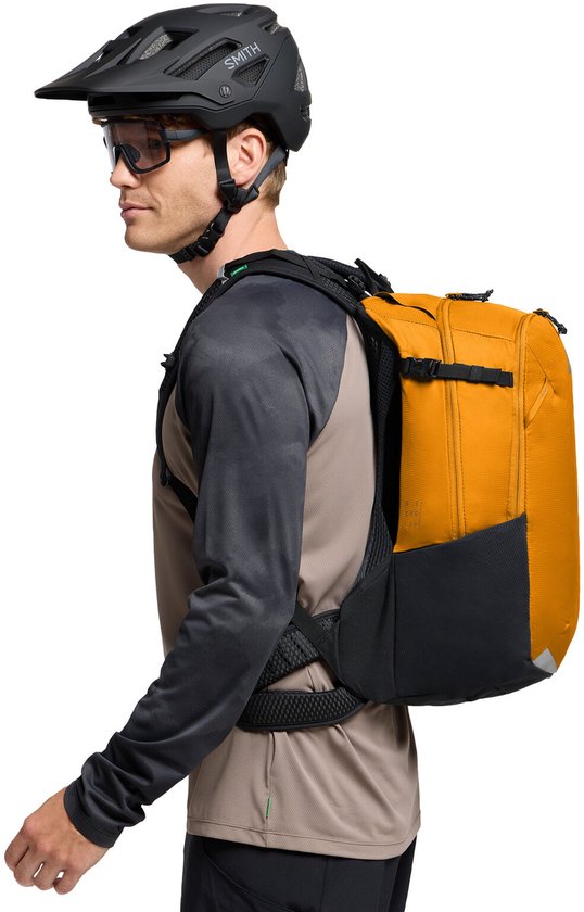Man met helm en bril draagt een oranje rugzak met zwart accent en reflecterende details.